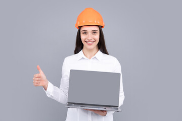 Hapy woman in protective hard hat helmet with laptop computer isolated on grey background. Architect woman wear helmet and shirt. Business woman, construction manager, builder.