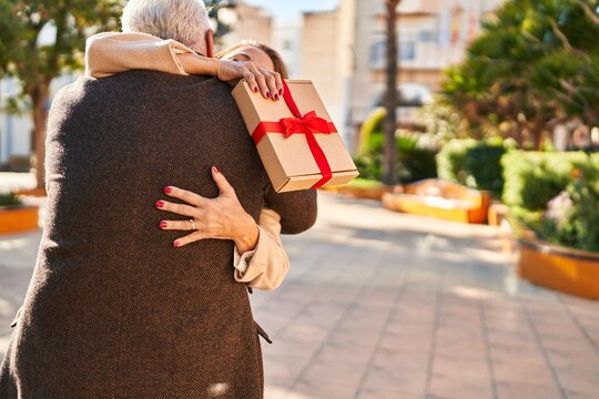 Middle age man and woman couple hugging each other holding gift at park