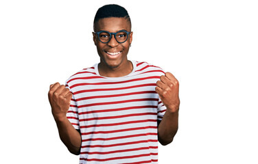 Naklejka premium Young african american man wearing casual t shirt and glasses celebrating surprised and amazed for success with arms raised and open eyes. winner concept.