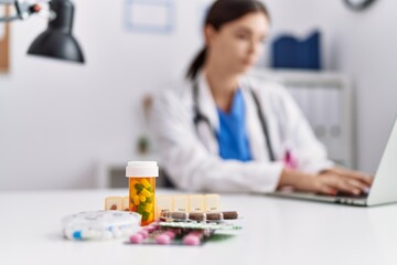 Fototapeta premium Young hispanic woman wearing doctor uniform prescribing pills at hospital