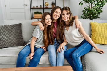 Three young hispanic woman smiling happy and hugging sitting on the sofa at home.