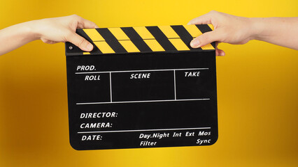 Two hands send and hold a Black clapper board or movie slate on yellow background.