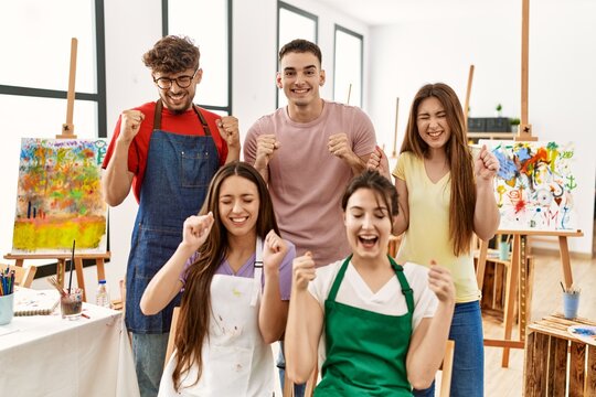 Group of five hispanic artists at art studio excited for success with arms raised and eyes closed celebrating victory smiling. winner concept.