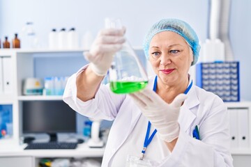 Middle age blonde woman wearing scientist uniform holding test tube at laboratory