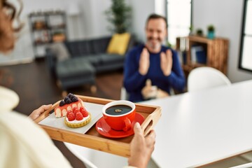 Woman holding tray with breakfast surprising her husband at home.