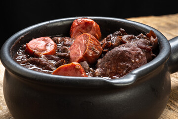 FEIJOADA served in a clay bowl on a rustic wooden table