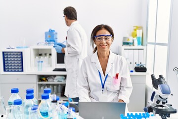 Middle age woman working at scientist laboratory looking positive and happy standing and smiling with a confident smile showing teeth