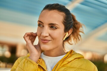 Young hispanic girl smiling happy using earphones at the city.