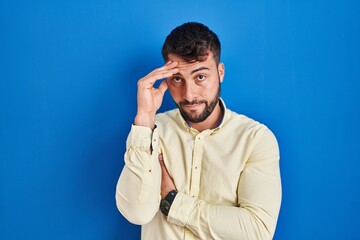 Handsome hispanic man standing over blue background worried and stressed about a problem with hand on forehead, nervous and anxious for crisis