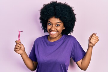 Young african american woman holding razor screaming proud, celebrating victory and success very...