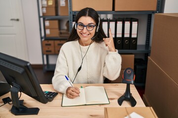 Young hispanic woman working at small business ecommerce wearing headset smiling with an idea or question pointing finger with happy face, number one