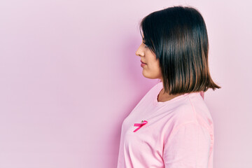 Young hispanic woman wearing pink cancer ribbon on t shirt looking to side, relax profile pose with natural face and confident smile.