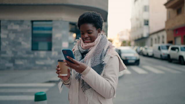 Young african american woman using smartphone drinking coffee at street