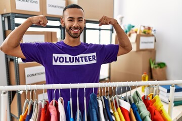 African american man wearing volunteer t shirt at donations stand showing arms muscles smiling proud. fitness concept.
