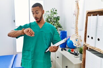 African american physiotherapist man working at pain recovery clinic looking at the watch time...