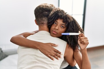 Young interracial couple holding pregnancy test result thinking attitude and sober expression...