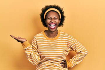Young african american woman presenting with open palms, holding something smiling and laughing...