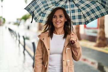 Middle age woman smiling confident using umbrella at street