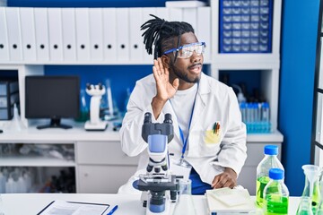 African man with dreadlocks working at scientist laboratory smiling with hand over ear listening...