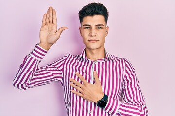 Young hispanic man wearing casual clothes swearing with hand on chest and open palm, making a...