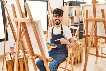 Hispanic man with beard at art studio smiling happy pointing with hand and finger