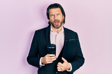 Middle age caucasian man wearing business clothes drinking a take away cup of coffee in shock face,...