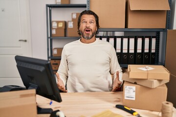 Handsome middle age man working at small business ecommerce afraid and shocked with surprise expression, fear and excited face.