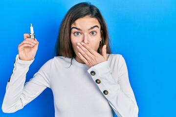 Young caucasian girl holding spark plug covering mouth with hand, shocked and afraid for mistake....