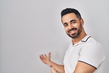 Young hispanic man with beard wearing casual clothes over white background inviting to enter smiling natural with open hand