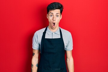 Young hispanic man wearing apron afraid and shocked with surprise expression, fear and excited face.