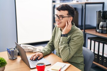 Young non binary man business worker using laptop listening to music at office
