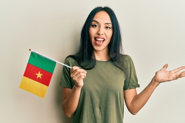 Young hispanic girl holding cameroon flag celebrating achievement with happy smile and winner...