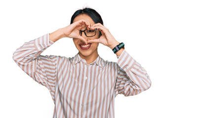 Young hispanic girl wearing casual clothes and glasses doing heart shape with hand and fingers smiling looking through sign