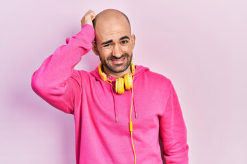 Young bald man wearing gym clothes and using headphones confuse and wonder about question....