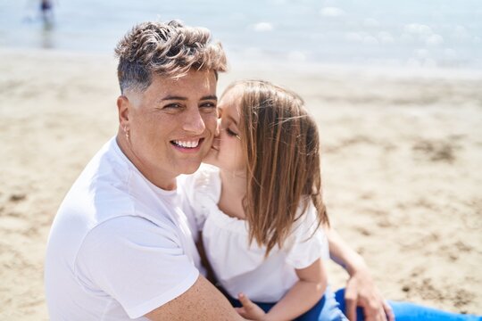 Father and daughter kissing and hugging each other sitting on sand at beach
