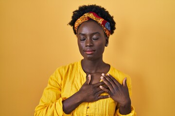 African young woman wearing african turban smiling with hands on chest with closed eyes and grateful gesture on face. health concept.