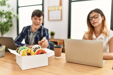 Two business workers smiling happy eating doughnuts at the office.