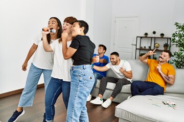Group of young friends having party singing song using microphone at home.