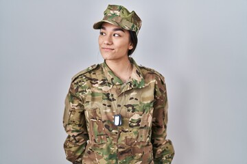 Young south asian woman wearing camouflage army uniform smiling looking to the side and staring...