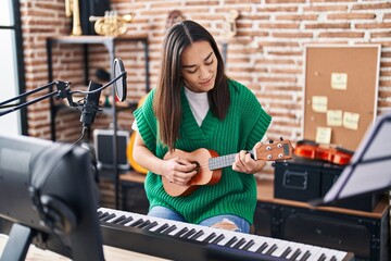 Fototapeta na wymiar Young hispanic woman musician playing ukulele at music studio