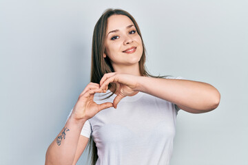 Young hispanic girl wearing casual white t shirt smiling in love doing heart symbol shape with hands. romantic concept.