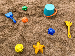 Fototapeta na wymiar Top view of bright colored plastic molds, shovel, rake and bucket in the sandbox, against the background of dark sand with raindrops. Copy space