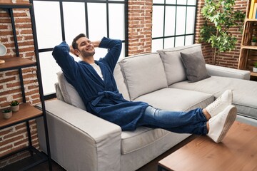 Young hispanic man wearing bathrobe relaxed with hands on head at home - obrazy, fototapety, plakaty