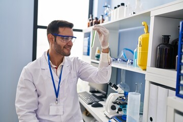 Young hispanic man scientist looking test tube at laboratory