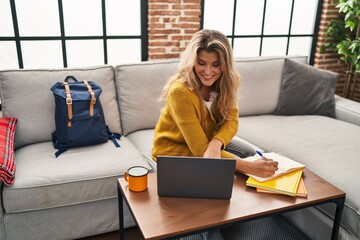 Young blonde woman smiling confident studying using laptop at home