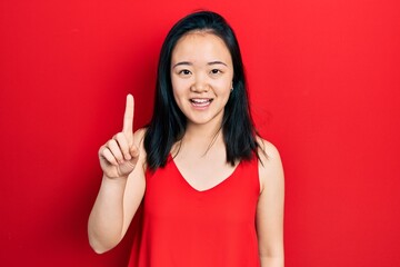 Young chinese girl wearing casual clothes smiling with an idea or question pointing finger up with happy face, number one