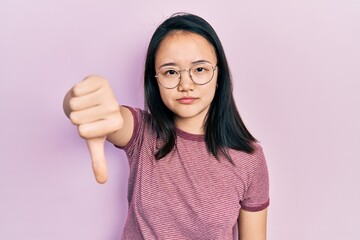Young chinese girl wearing casual clothes and glasses looking unhappy and angry showing rejection and negative with thumbs down gesture. bad expression.