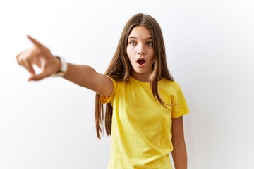 Young brunette teenager standing together over isolated background pointing with finger surprised ahead, open mouth amazed expression, something on the front