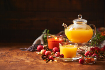 Glass teapot and cup with sea buckthorn tea with spices and autumn small crabapples on wooden background