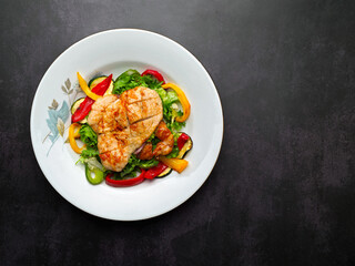 Roasted chicken and vegetable salad, with black background and white plate